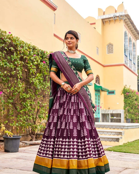 Woman in a traditional outfit with a patterned skirt and purple blouse standing outdoors.