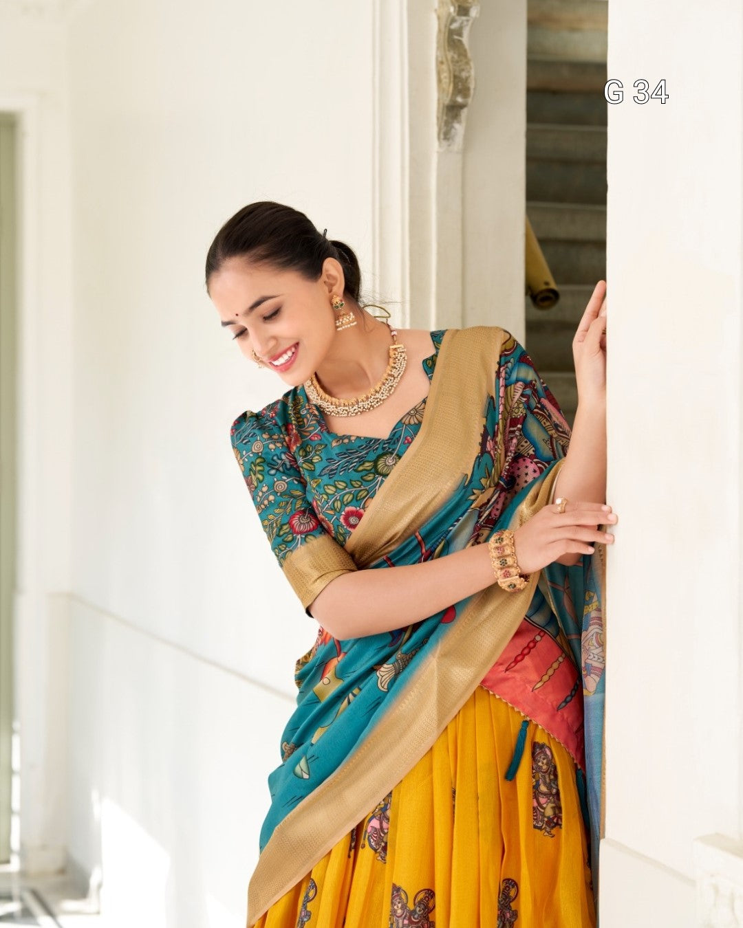 Woman in a colorful saree with jewelry, standing indoors.
